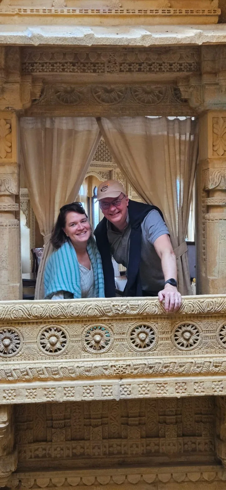 Two smiling travelers leaning over an intricately carved stone balcony